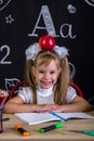 Cheerful and happy hellion schoolgirl sitting at the desk with books, school supplies, with a red apple on the top of