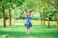 Cheerful and happy little girl with arms outstretched summer in a blue dress outdoors in a park smiles sweetly.