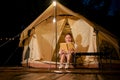Asian female camping at the campground, sits in front of her tent and reading a novel at night