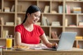 Cheerful happy young asian lady student watch online lesson on laptop, chatting and have breakfast Royalty Free Stock Photo