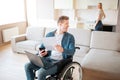 Cheerful happy young man with special needs look back. Holding laptop an piece of paper. Young woman stand at stove and