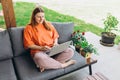 Cheerful happy young redhead woman relaxing with laptop in the yard of the house in summer. Casual beautiful woman is Royalty Free Stock Photo