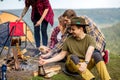 Cheerful hikers roasting mushroom while having picnik
