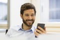 Cheerful Hipster man in office. Typing text message on mobile ph