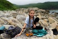 Cheerful hipster teen girl enjoying camp halt at stones beach relaxing cooking food on gas burning Royalty Free Stock Photo