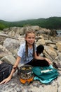 Cheerful hipster teen girl enjoying camp halt at stones beach relaxing cooking food on gas burning Royalty Free Stock Photo