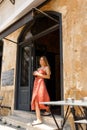 Cheerful hipster young woman in skirt go out from stylish cafe place,old city street drinking,holding cup of morning Royalty Free Stock Photo