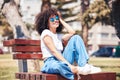 Cheerful hispanic woman wearing sunglasses and sitting on a park bench outside. Carefree young woman with a curly afro Royalty Free Stock Photo