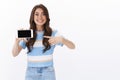 Cheerful impressed enthusiastic young woman cannot wait play new smartphone game, hold mobile phone, pointing horizontal