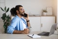 Cheerful Indian Freelancer Guy Resting With Coffee And Cellphone At Home Office Royalty Free Stock Photo