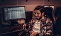 A young cheerful Indian guy wearing a military shirt sitting on a gamer chair in a gaming club or internet cafe.