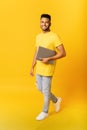 Cheerful Indian man carrying laptop computer isolated on yellow. Happy arab male student with laptop, freelancer using Royalty Free Stock Photo