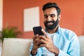 Cheerful Indian Man Using Mobile Phone Surfing Internet Sitting Indoor Royalty Free Stock Photo