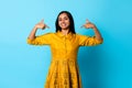 Cheerful Indian woman pointing fingers at herself over blue background