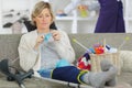 Cheerful injured woman knitting on sofa