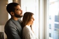 Cheerful international millennial couple hugging, look out the window, enjoy free time together