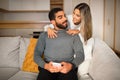 Cheerful international millennial couple hugging looking at smartphone in living room interior