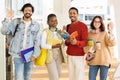 Cheerful international millennial students exchange, with books and coffee, waving hands at campus