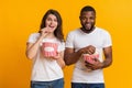 Cheerful interracial couple eating popcorn, enjoying cinema snack over yellow background