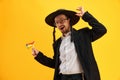 Cheerful Jewish man in hat, with sidelocks holding noisemaker, against yellow background. Celebration