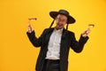 Cheerful Jewish man in hat, with sidelocks holding noisemaker, against yellow background. Celebration