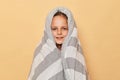 Cheerful joyful smiling little girl wrapped in striped blanket isolated over beige background lookign at camera waking up at lazy Royalty Free Stock Photo