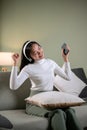 A joyful Asian woman is enjoying the music and dancing while sitting on a sofa in her living room Royalty Free Stock Photo