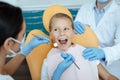 Cheerful kid looks at doctor sits in chair, lady dentist in protective mask and rubber gloves start to treats teeth