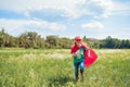cheerful kid in red superhero cape and mask running in meadow