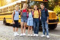 Cheerful kids with backpacks standing by yellow school bus, smiling and embracing Royalty Free Stock Photo