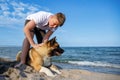 Teenage guy with blond hair and leash in hands plays and walks with dog of Akina Inu breed on wild beach along Black Sea Royalty Free Stock Photo