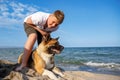 Teenage guy with blond hair and leash in hands plays and walks with dog of Akina Inu breed on wild beach along Black Sea Royalty Free Stock Photo