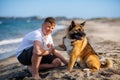 Teenage guy with blond hair and leash in hands plays and walks with dog of Akina Inu breed on wild beach along Black Sea Royalty Free Stock Photo