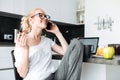 Cheerful lady laughing while talking on smartphone in kitchen Royalty Free Stock Photo