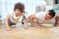 Cheerful latin boy smiling at camera while exercising together with his sportive middle aged father, doing push ups at