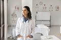 Cheerful Latin doctor with stethoscope on neck looking at away