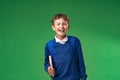 Cheerful laughing schoolboy holding book and backpack on green background