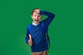 Cheerful laughing schoolboy holding book and backpack on green background