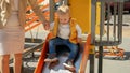 Cheerful laughing toddler boy holding mother's hand and sliding down on the playground