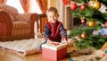 Portrait of cheerful laughing toddler boy opening Christmas gift box while sitting on the floor under Christmas tree Royalty Free Stock Photo