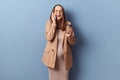 Cheerful laughing young adult pregnant woman wearing dress and jacket posing isolated over blue background talking on mobile phone Royalty Free Stock Photo