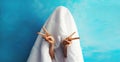 Cheerful lazy woman waking up after sleeping covered head with white blanket showing cool gesture her fingers on blue background