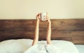 Cheerful lazy woman waking up after sleeping lying in soft comfortable bed showing empty cup coffee stretching her hands up from