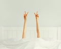 Cheerful lazy woman waking up after sleeping lying in soft comfortable bed showing gesture stretching her hands up from under the