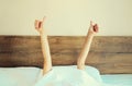 Cheerful lazy woman waking up after sleeping lying in soft comfortable bed showing gesture stretching her hands up from under the