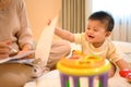 Cheerful little baby boy sitting on the bed near busy mother working on laptop Royalty Free Stock Photo