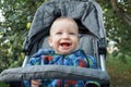 A cheerful little baby up to a year old is sitting in a stroller and happy smiling laughing and playing with his parents on the st Royalty Free Stock Photo