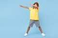 Cheerful little boy with african with headphones dabbing with one leg on soccer ball over blue background.