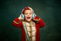 Cheerful little boy dressed up as medieval little prince and pageboy listening to music over dark vintage style