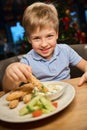 Cheerful little boy eating French fries with nuggets during New Year celebration Royalty Free Stock Photo